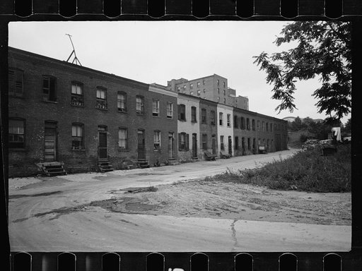 Block of slum houses with outside toilets and water supply, hotel to the left and the round roof of Union Station in the right background, Washington, D.C.