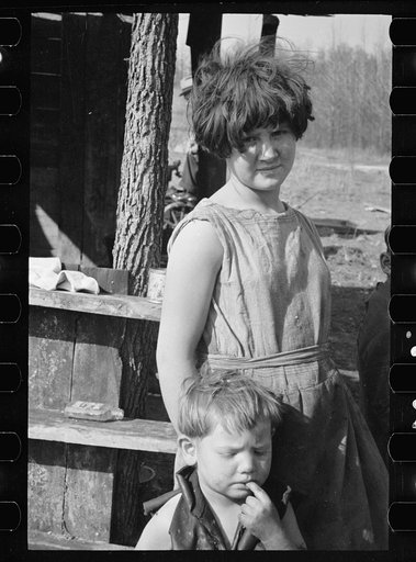 Twelve-year old girl of family of nine living in one-room hut built over the chassis of abandoned Ford truck in open field on U.S. Route 70 between Camden and Bruceton, Tennessee. Near backward Tennessee section. View also shows one of the small boys in family; the girl is dressed in a meal sack