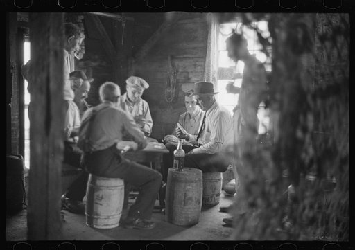 Untitled photo, possibly related to: Fishermen in repair shack repairing nets and sharpening tools. The twine of these nets is impregnated with coal tar; as the sewing of nets requires the holding of the twine in the mouth an occupational disease has developed which is referred to as fishermen's lip