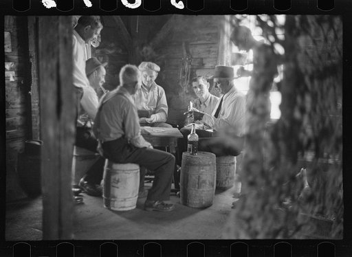 Untitled photo, possibly related to: Fishermen in repair shack repairing nets and sharpening tools. The twine of these nets is impregnated with coal tar; as the sewing of nets requires the holding of the twine in the mouth an occupational disease has developed which is referred to as fishermen's lip