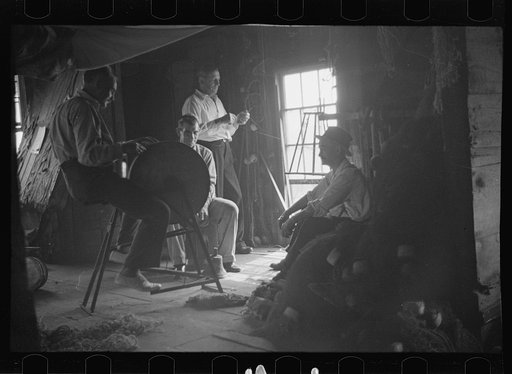Fishermen in repair shack repairing nets and sharpening tools. The twine of these nets is impregnated with coal tar; as the sewing of nets requires the holding of the twine in the mouth an occupational disease has developed which is referred to as fishermen's lip cancer. Provincetown, Massachusetts