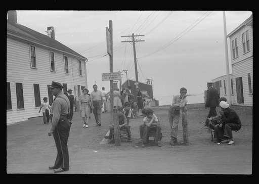 Entrance to the town pier before the arrival of the Boston boat. The policeman is an institution, knows everybody, even every summer visitor. The boys wait for the chance of carrying somebody's baggage. Provincetown, Massachusetts