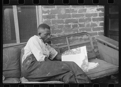 Negro reading in front of his alley dwelling home, Washington, D.C.