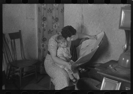 Child on lap of mother reading the newspaper. Nissen shack near Dickens, Iowa