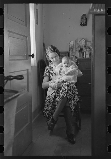 Untitled photo, possibly related to: Child on lap of mother reading the newspaper. Nissen shack near Dickens, Iowa