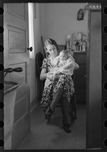 Untitled photo, possibly related to: Child on lap of mother reading the newspaper. Nissen shack near Dickens, Iowa