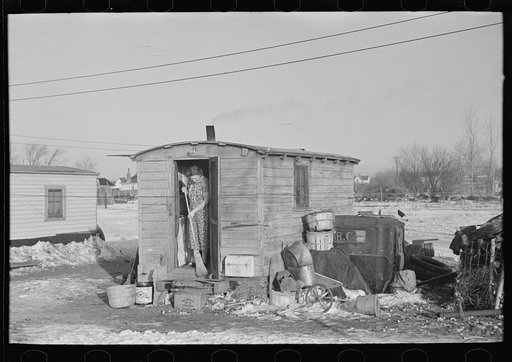 Mrs. Charles Benning sweeping steps of shack in "Shantytown," Spencer, Iowa