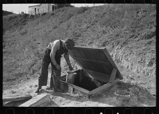 Herman Gerling dipping water from a spring to fill the barrels on his truck. North Dakota