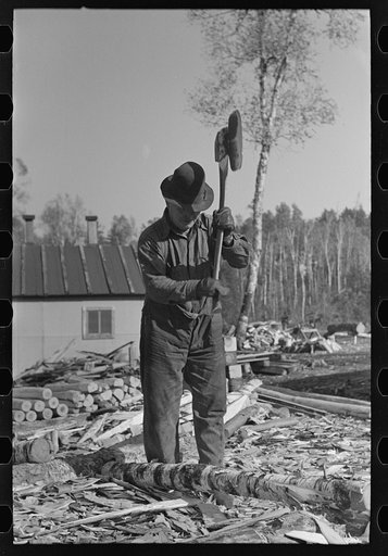 Lumberjack using a broadaxe at camp near Effie, Minnesota