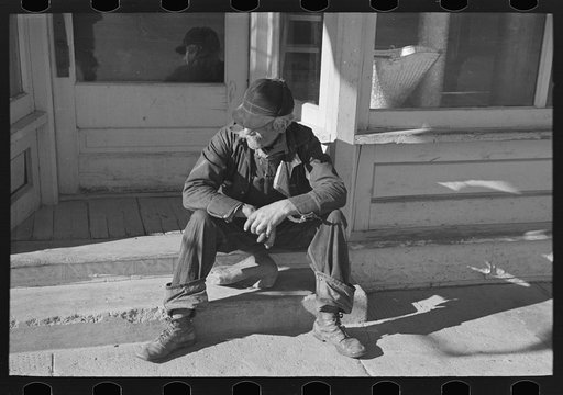 Arnegard, McKenzie County, North Dakota. Old man sitting on a store step