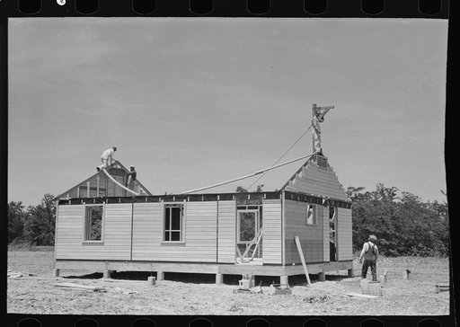 Southeast Missouri Farms Project. House erection. After exterior wall panels are in place gable ends are lifted up by means of a gin pole. This was necessary for safety purposes because of strong winds