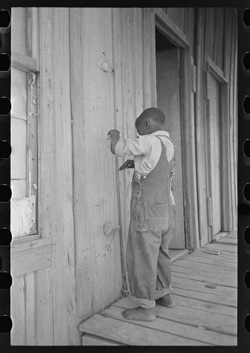 Child of former sharecropper, playing primitive musical instrument made by stretching wire from one nail to another creating sort of violin. Southeast Missouri Farms