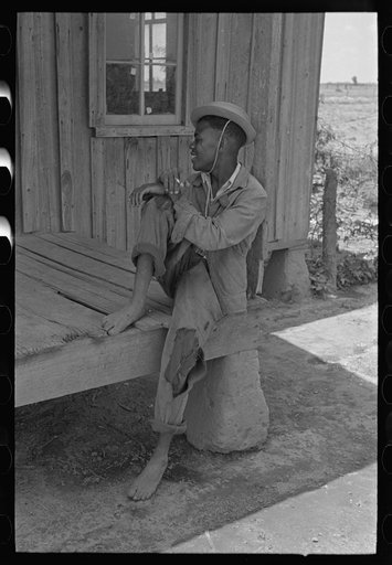 Son of sharecropper sitting on front porch of shack home, New Madrid County, Missouri