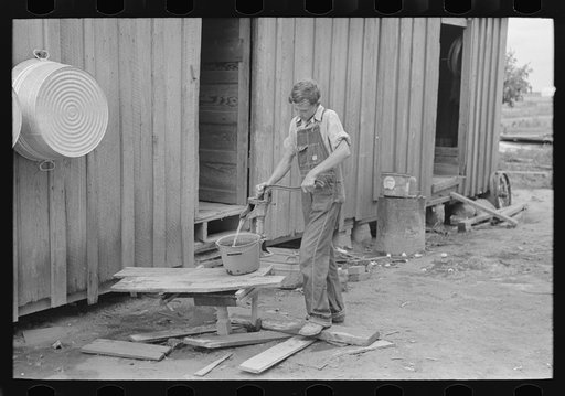 Son of sharecropper pumping water in rear of cabin home, New Madrid County, Missouri