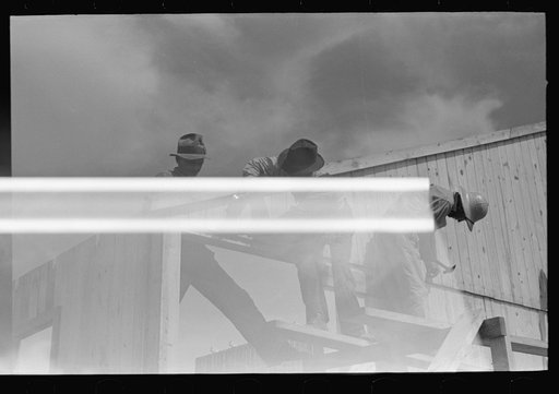 Untitled photo, possibly related to: Barn erection. Sliding last half of one gable end into place. Note that gable end sheathing overlaps sheathing of wall panels, forming a drip. Southeast Missouri Farms Project