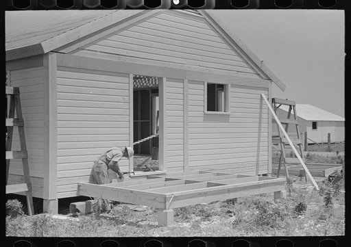Southeast Missour Farms Project. House erection.  Shop-assembled porch floor being fastened into place. Note that trim and batten strips are already in place on the house