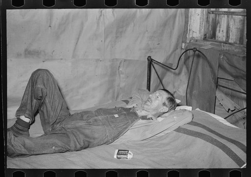 Squatter resting on bed in abandoned warehouse; he was in ill health. Caruthersville, Missouri