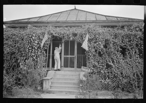 Man taking up flag in front of house to provide local atmosphere for state fair, Donaldsonville, Louisiana