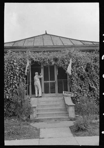 Untitled photo, possibly related to: Man taking up flag in front of house to provide local atmosphere for state fair, Donaldsonville, Louisiana