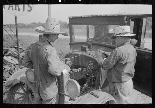 Farmer watching junkyard owner examining condition of spark coils in model-T Ford, Abbeville, Louisiana