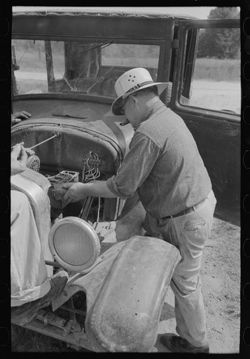 Junkyard owner working on automobile of farmer near Abbeville, Louisiana
