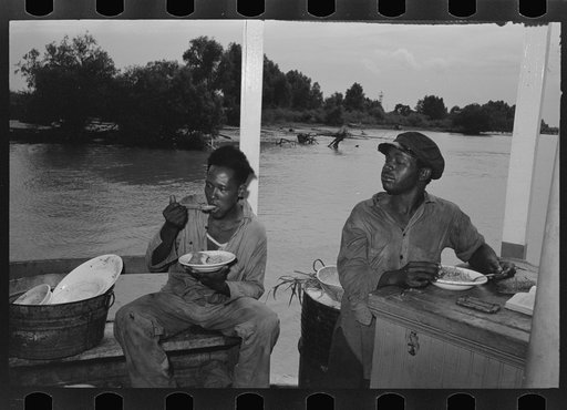 Negro stevedores eating on stern of boat. Food supplied to crew consists almost entirely of carbohydrates with some of the cheaper cuts of meat. Sleeping quarters are not provided for stevedores, who sleep in any available space. Aboard El Rito, Pilottown, Louisiana