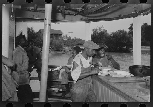 Negro stevedores eating on stern of boat. Food supplied to crew consists almost entirely of carbohydrates with some of the cheaper cuts of meat. Sleeping quarters are not provided for stevedores, who sleep in any available space. Aboard El Rito, Pilottown, Louisiana