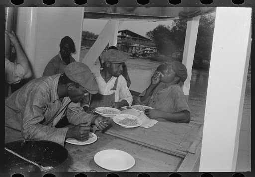 Negro stevedores eating on stern of boat. Food supplied to crew consists almost entirely of carbohydrates with some of the cheaper cuts of meat. Sleeping quarters are not provided for stevedores, who sleep in any available space