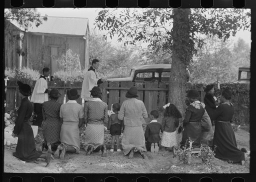 Negroes kneeling at graves of relatives, and being blessed by priest with holy water, New Roads, Louisiana
