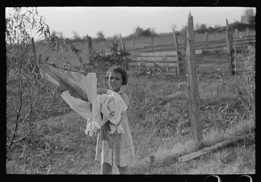 Daughter of Cajun cane farmer removing clothes from line near New Iberia, Louisiana