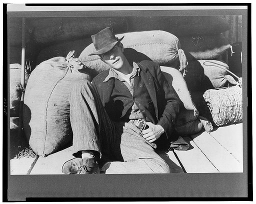 Man resting on sack of grain near barbed wire, New Roads, Louisiana