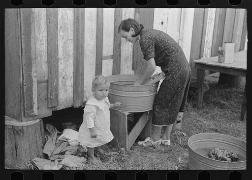 Farmer's wife washing clothes and watching son at same time. Note construction of house. Near Morganza, Louisiana. Mrs. W.E. Smith