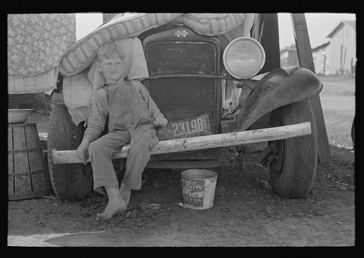 Son of white migrant sitting on bumper of their truck, Weslaco, Texas. Notice New Mexico license