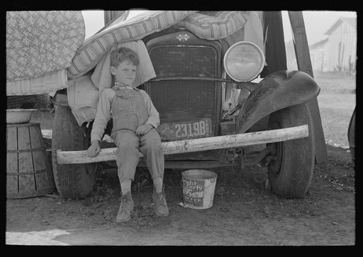 Son of white migrant sitting on bumper of their truck, Weslaco, Texas. Notice New Mexico license