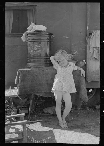 Child of migrant family in front of household goods of trailer home, Weslaco, Texas