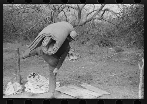 White migrant carrying mattress across fence near Harlingen, Texas