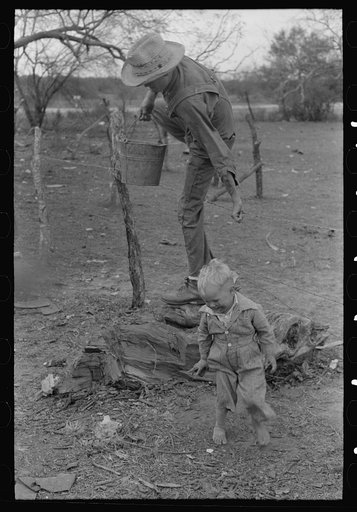 Child of white migrant climbing fence with pail of water near Harlingen, Texas