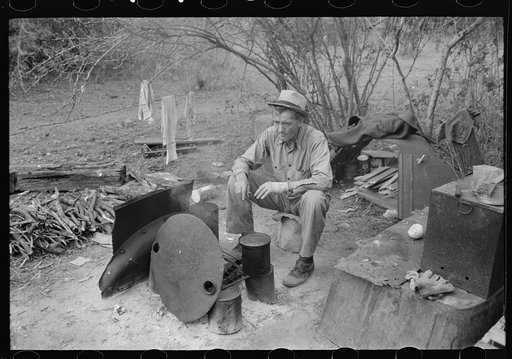 White migrant worker sitting in front of fire. He lived with two other white men migrant workers. He was a Texan. Harlingen, Texas