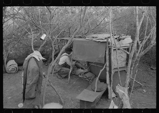 White migrant worker living in camp with two other men, working on lean-to which is to be his sleeping quarters. Near Harlingen, Texas