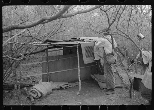 White migrant worker living in camp with two other men, working on lean-to which is to be his sleeping quarters. Near Harlingen, Texas