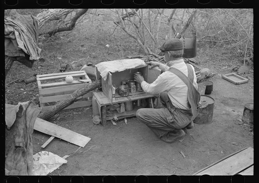 White migrant in camp near Harlingen, Texas. He is one of the three traveling separately but who have set up camp together. Each cooks and eats alone. They were attracted to the lower valley by reports of plentiful work, but have been unable to compete with the local Mexican labor in that section