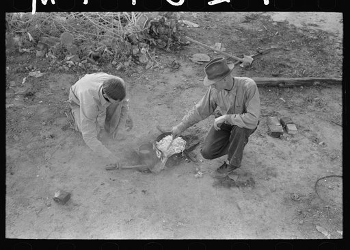 Migrant father and son cooking meal over campfire, Edinburg, Texas