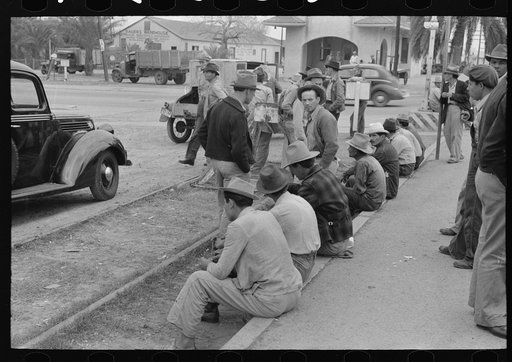 Men sitting along railroad platform waiting for work as day laborers, Raymondville, Texas