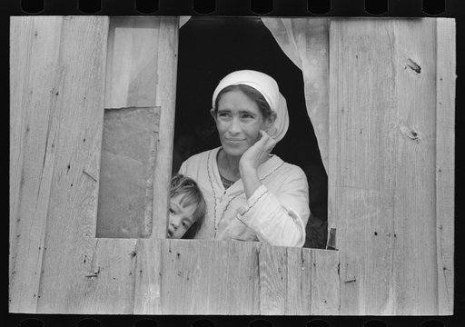 Mexican woman and son looking out of window into corral, San Antonio, Texas