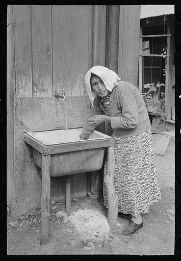 Old Mexican woman drawing water at community hydrant, San Antonio, Texas