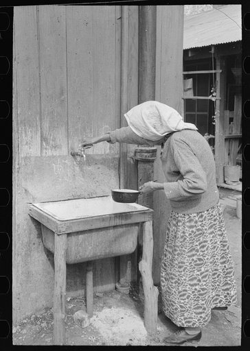Old Mexican woman drawing water from community hydrant, San Antonio, Texas