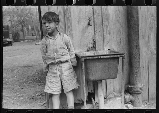 Mexican boy in front of community water hydrant and sink, San Antonio, Texas