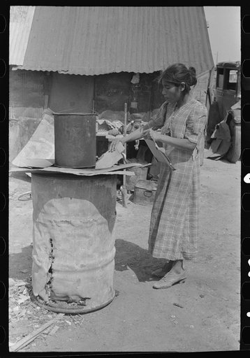 Mexican woman building fire in battered steel drum in backyard of her house, San Antonio, Texas
