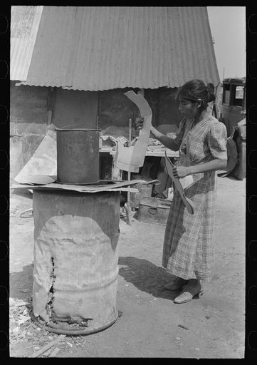 Untitled photo, possibly related to: Mexican woman building fire in battered steel drum in backyard of her house, San Antonio, Texas