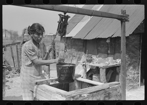 Mexican woman drawing a bucket of water from backyard well, San Antonio, Texas